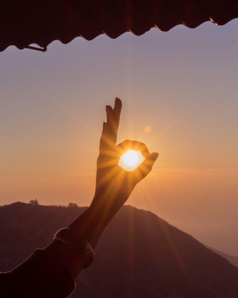 A hand frames the sun at sunset over the Thoptewadi hills, India.